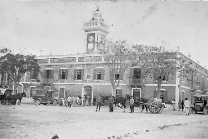 Ayuntamiento de Villa Carlos, años 20. De izquierda a derecha, carruaje de servicio público. Omnibus de 20 plazas. Carro o cuba de reparto de agua y otro coche de línea - Archivo M. Caules