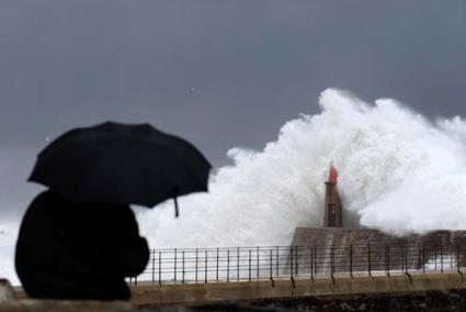 Oleaje. Un hombre mira las olas que baten contra un faro en la localidad asturiana de Viavelez - Reuters