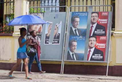 Guayana. Dos mujeres con parasol pasan frente a carteles electorales en Cayenne, camino de un colegio electoral - Reuters