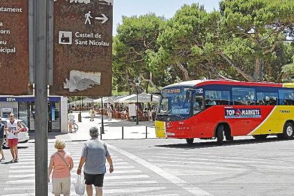 Una pareja de turistas cruza la calle frente a la parada de bus de Es Pins.