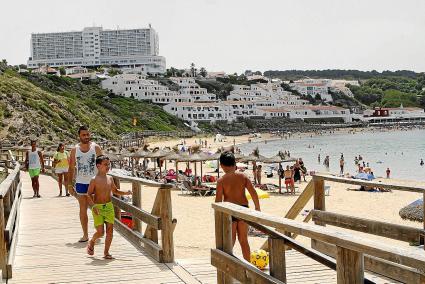 Arenal d’en Castell tarde con turistas, viviendas vacacionales sobre la playa y un hotel al fondo