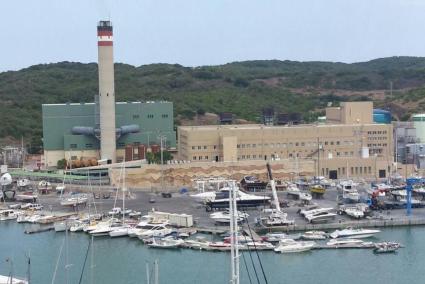 La central térmica de Endesa en el puerto de Maó, con los molinos del parque eólico de Milà detrás.