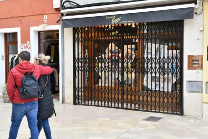 Una pareja pasa frente a una tienda cerrada con el escaparate cubierto de periódicos.