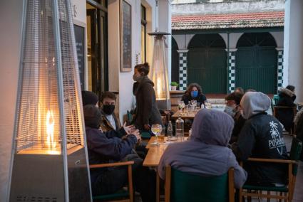 Un grupo de comensales en la terraza de un bar junto a una estufa de exterior.