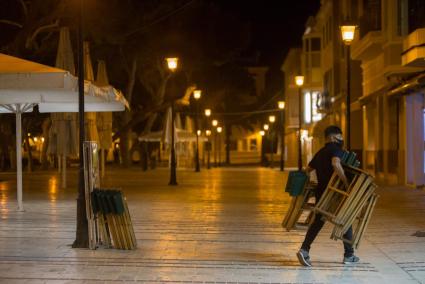 Un trabajador recoge las sillas de una terraza por la noche