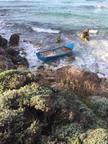 La embarcación varada entre rocas; al fondo, Els Brucs y Binigaus