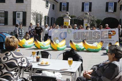 Manifestantes este sábado en la plaza Miranda de Maó, con pancartas por la equiparación del plus y plátanos hinchables en alusión al agravio respecto a Canarias