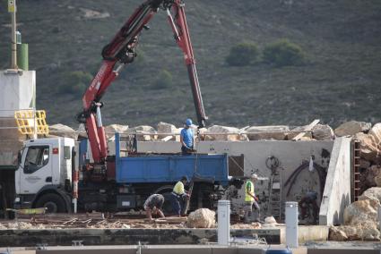 Un camión con grúa moviendo grandes piedras en la zona del muelle del puerto de Fornells