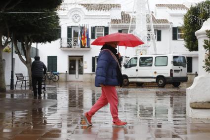 Una mujer camina con un paraguas por las calles de Sant Lluís.